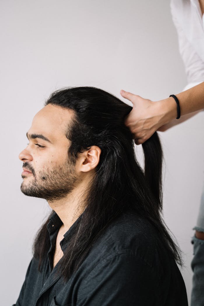 Profile of a man with long hair being styled into a ponytail.