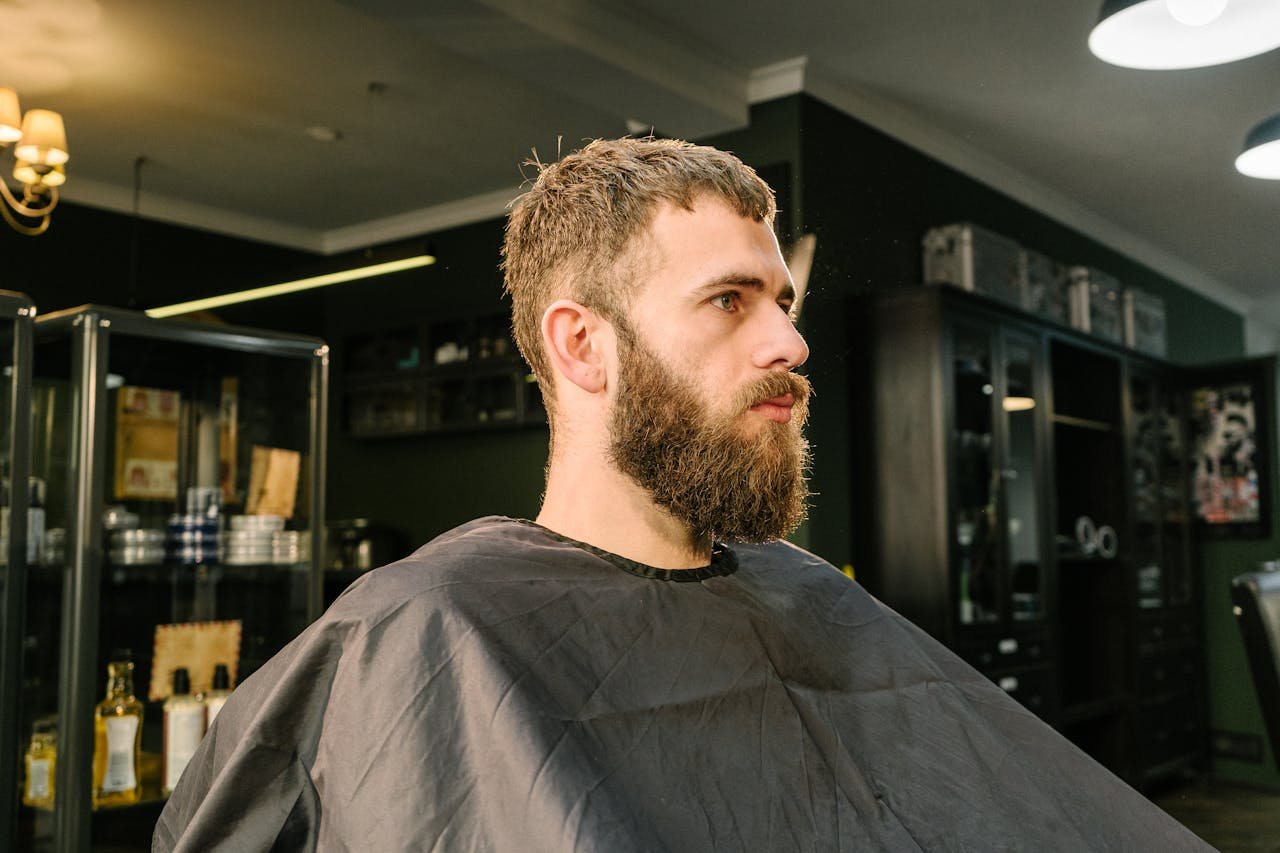 Bearded man sitting in a modern barbershop for a haircut and styling session.
